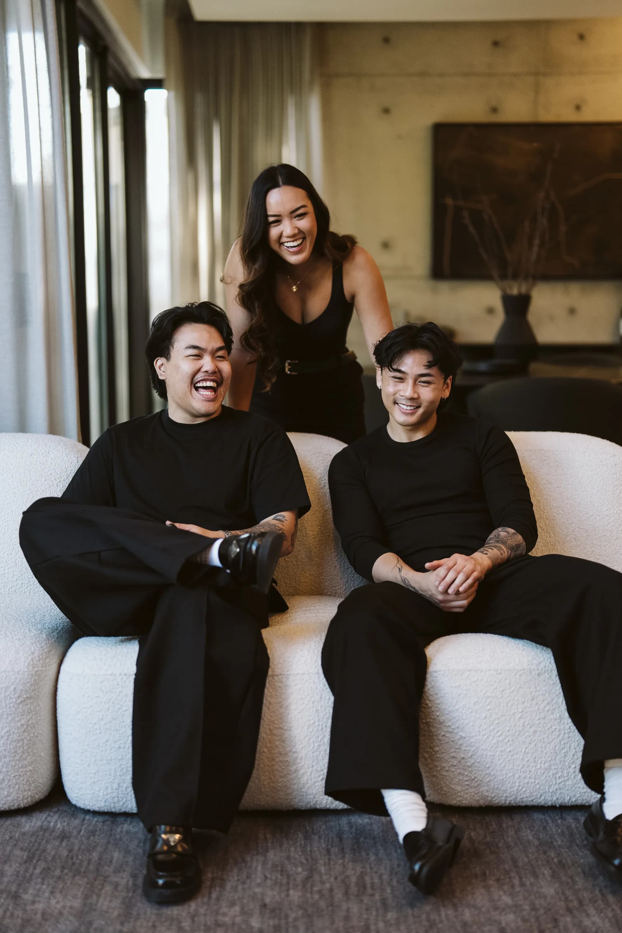 Three of the Revival Studios team on a white couch mid-laugh — two seated, one standing behind them.